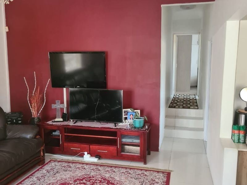 A living room featuring a bold red accent wall, crown molding, and tiled flooring, leading into a hallway.