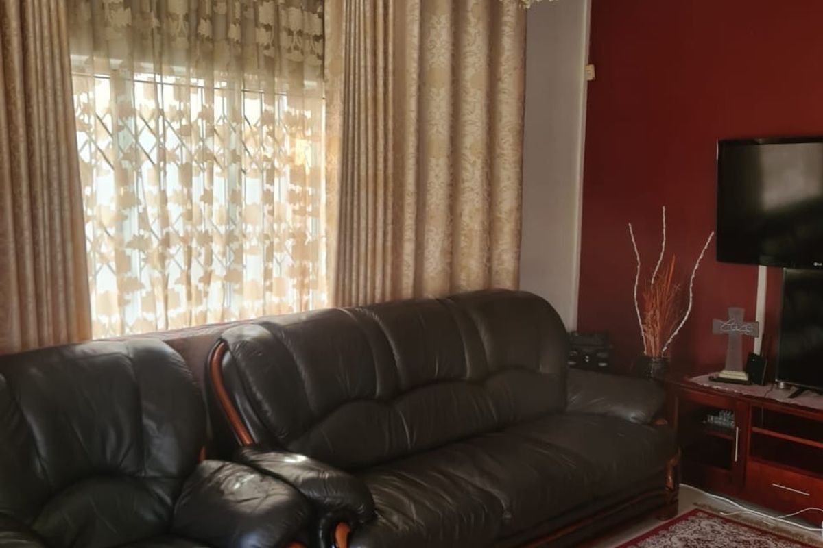 A living room featuring decorative ceiling cornicing, a crystal chandelier, and a window fitted with a security gate.