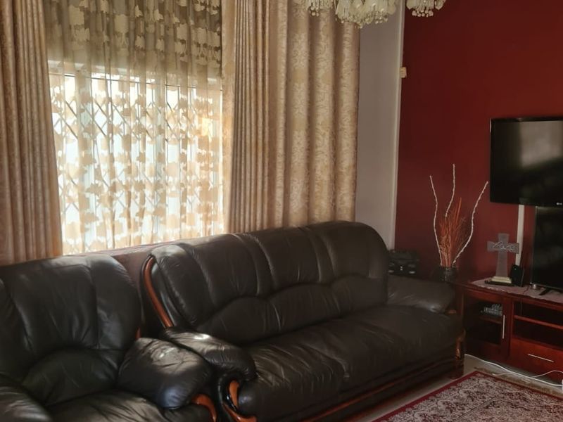 A living room featuring decorative ceiling cornicing, a crystal chandelier, and a window fitted with a security gate.