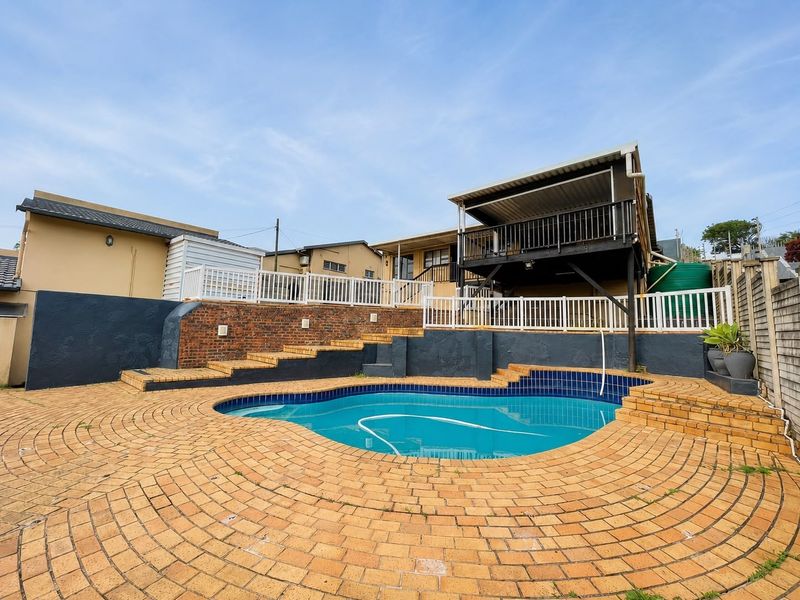 Outdoor pool area featuring a swimming pool, brick paved surround, raised deck with balustrade, and tiered retaining walls.