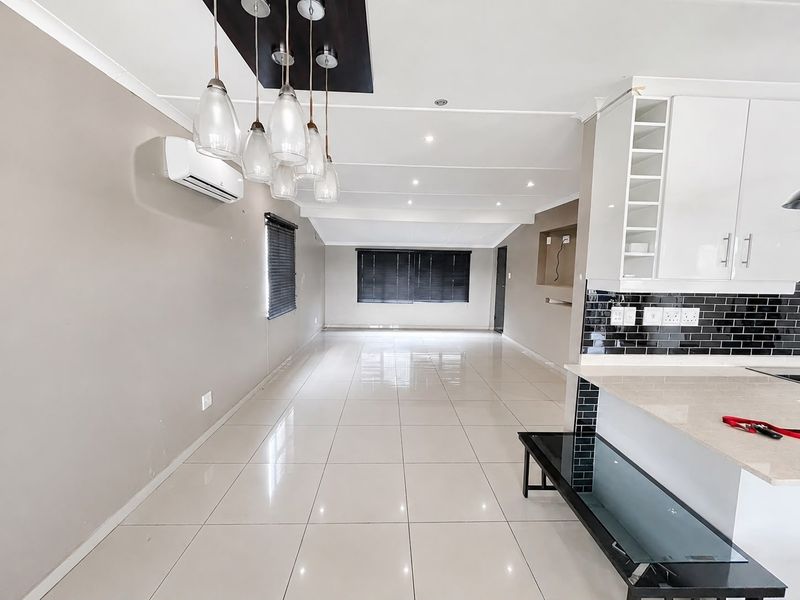 Spacious open-plan living and kitchen area featuring polished porcelain tiles, modern cabinetry, stone countertops, and integrated lighting throughout.