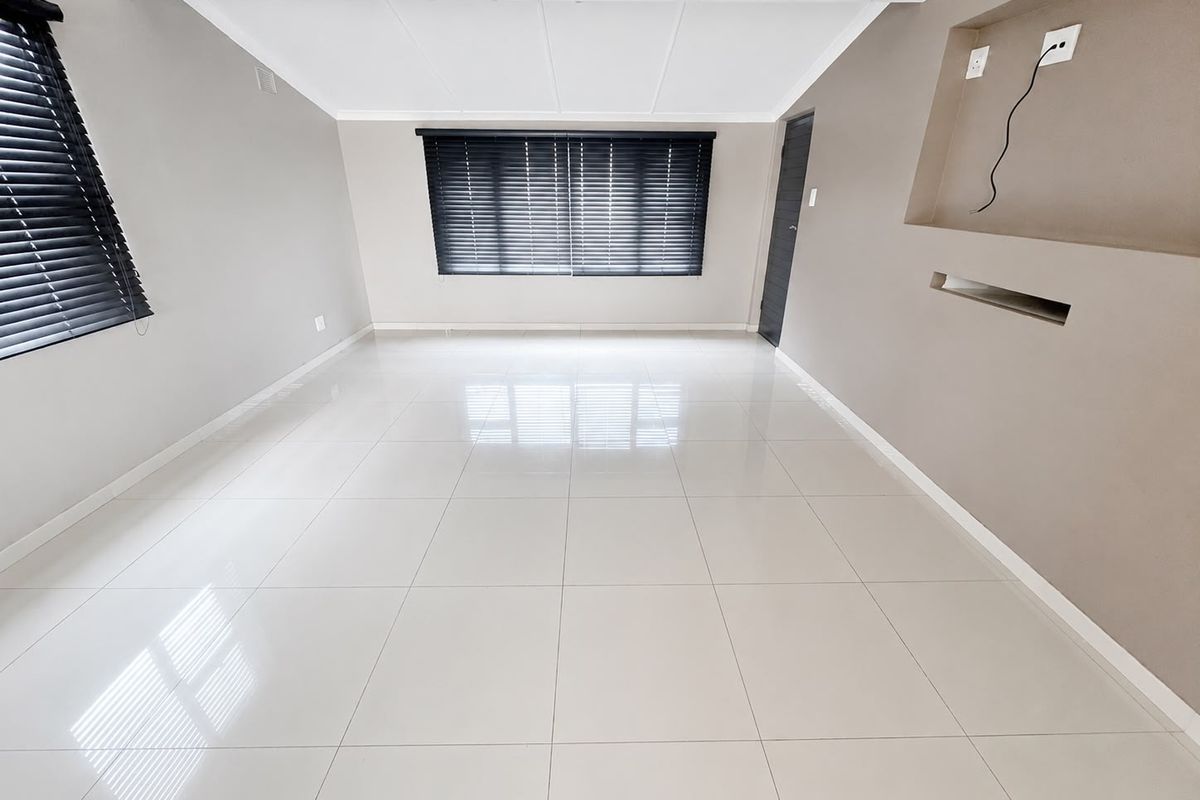 A bright, empty living room featuring polished floor tiles, a recessed wall niche for media, and modern venetian blinds.