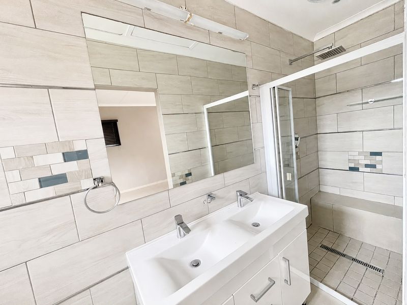 Modern bathroom featuring a double vanity, large wall-mounted mirror, and a spacious walk-in shower with a built-in bench and neutral tiling.