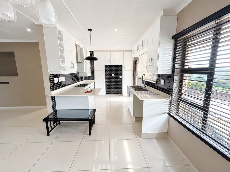 Modern kitchen featuring white gloss cabinetry, stone countertops, black subway tile backsplash, and integrated appliances with large windows and tiled flooring.
