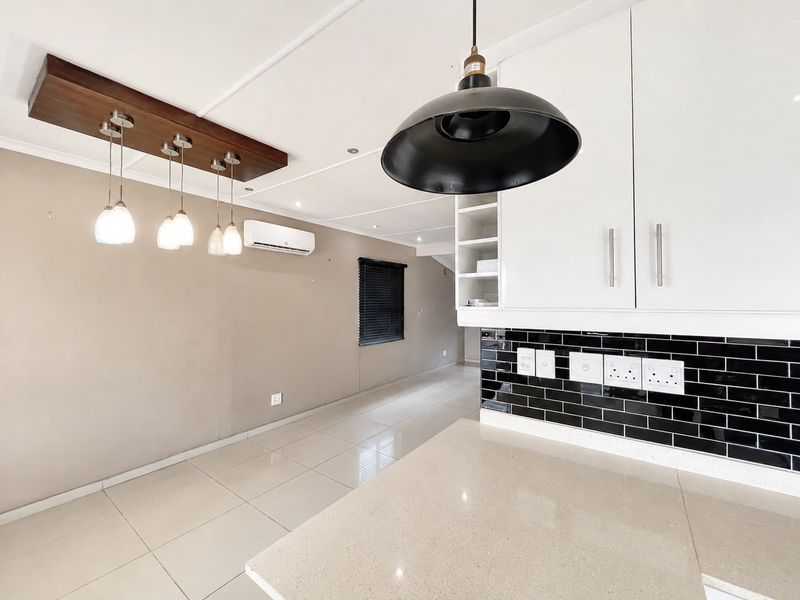 Modern kitchen area featuring sleek white cabinetry, black subway tile backsplash, quartz countertops, and tiled flooring, complemented by contemporary pendant lighting.