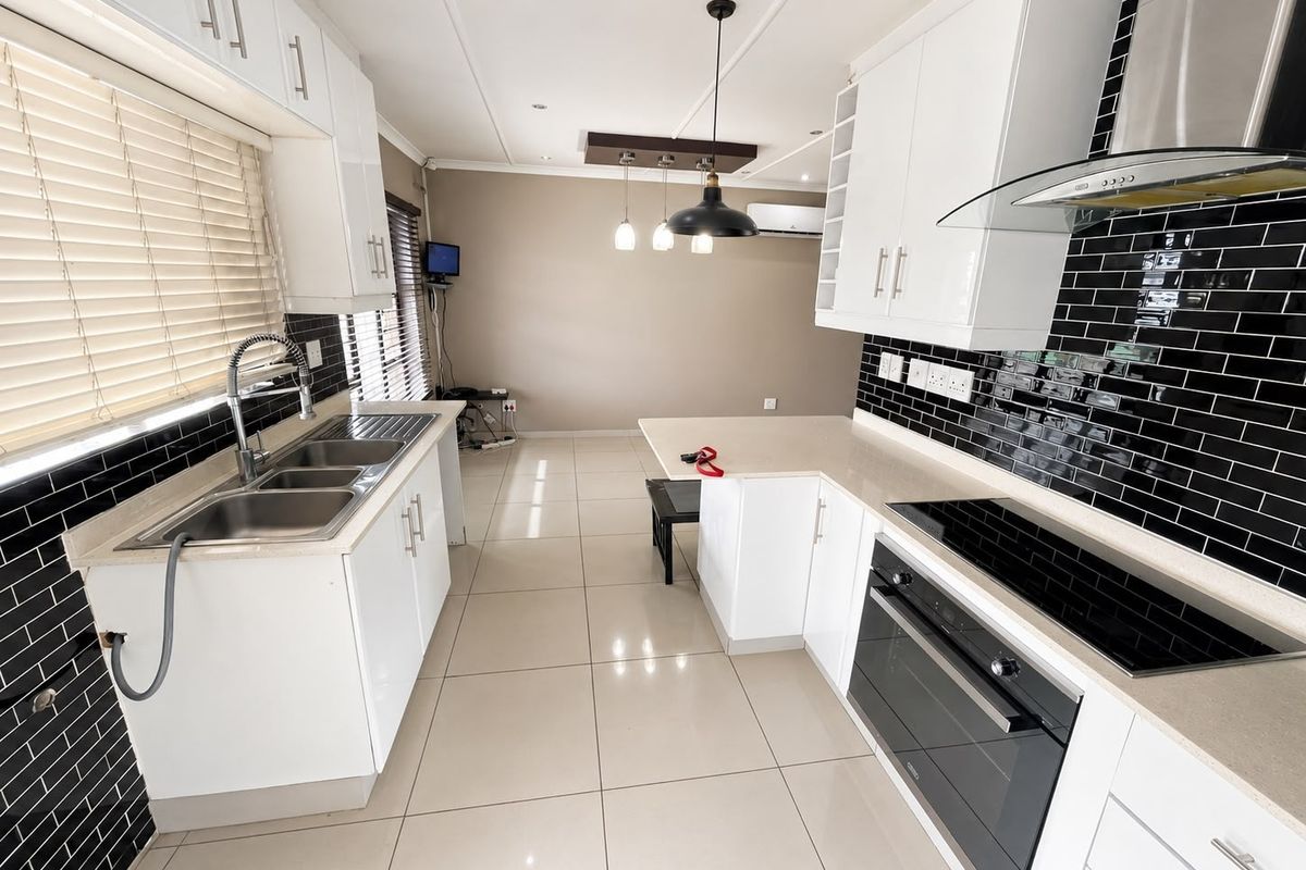 Modern kitchen featuring white cabinetry, stone countertops, black subway tile backsplash, integrated electric hob, oven, and extractor fan with tiled flooring.