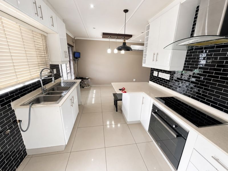 Modern kitchen featuring white cabinetry, stone countertops, black subway tile backsplash, integrated electric hob, oven, and extractor fan with tiled flooring.