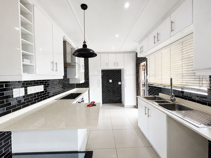 Modern, well-maintained kitchen featuring white gloss cabinetry, stone countertops, black subway tile backsplash, and high-quality stainless steel fixtures.
