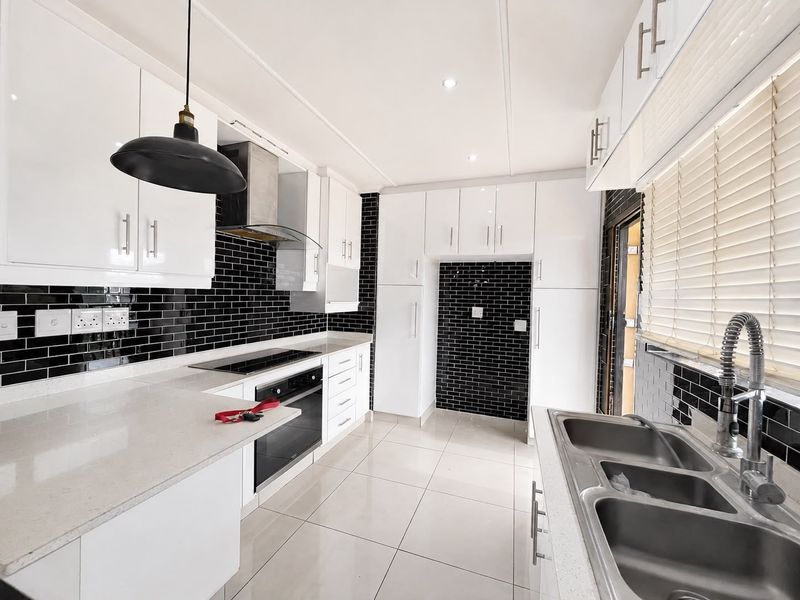 Modern kitchen featuring white gloss cabinetry, contrasting black subway tile backsplash, stone countertops, and high-quality stainless steel appliances.