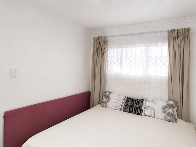 A functional bedroom featuring a window with security bars and neutral wall finishes.