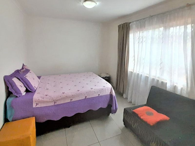 A functional bedroom featuring tiled flooring, a large window with security bars, and neutral wall finishes.