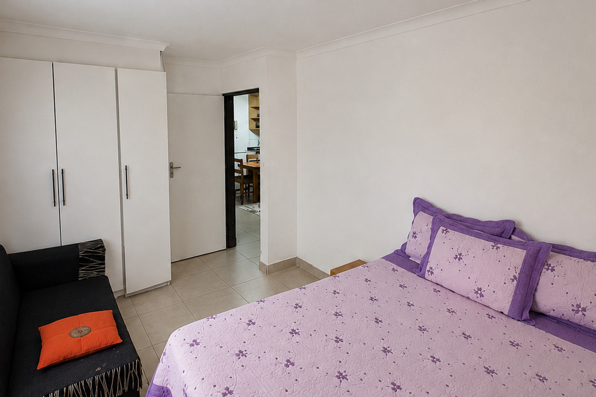 A bedroom featuring built-in wardrobes, tiled flooring, and coving, with a doorway leading to an adjacent living area.