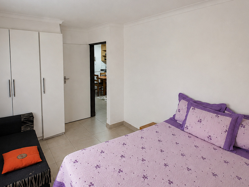 A bedroom featuring built-in wardrobes, tiled flooring, and coving, with a doorway leading to an adjacent living area.