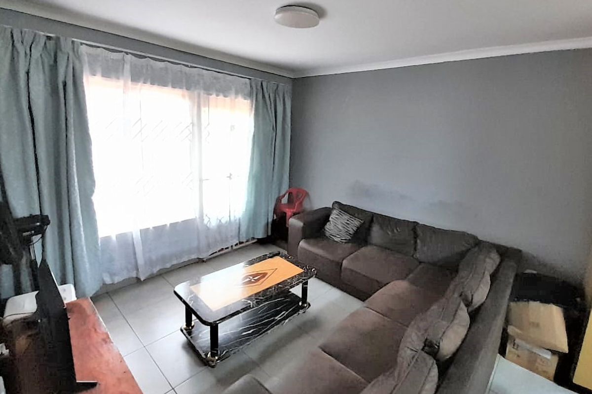 A living room featuring tiled flooring and a large sliding glass door providing natural light, with visible wall staining requiring attention.
