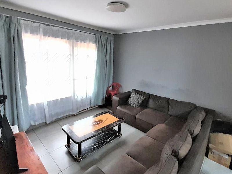 A living room featuring tiled flooring and a large sliding glass door providing natural light, with visible wall staining requiring attention.