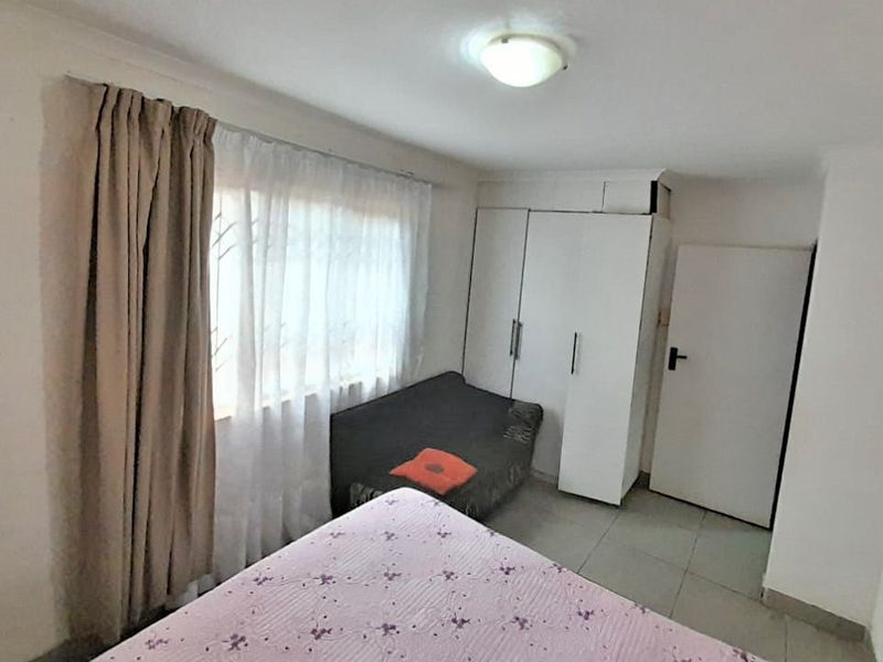 A functional bedroom featuring tiled flooring, a built-in wardrobe, and security bars on the window.
