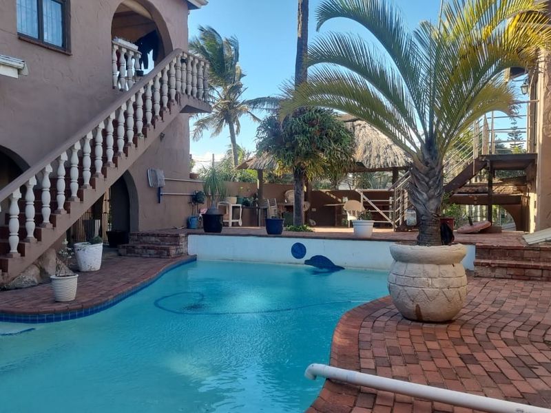 Outdoor pool area featuring brick paving, a balustrade staircase, and a thatched lapa structure in the background.