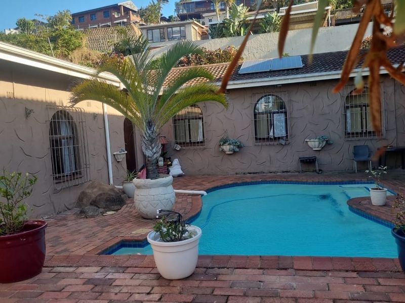 A private courtyard area featuring a swimming pool, brick paved surround, and exterior walls with arched windows and security bars.