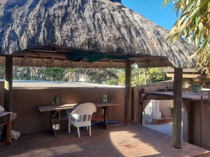 Covered outdoor patio area featuring a traditional thatch roof, timber support posts, and brick paving, providing a rustic space for outdoor relaxation.