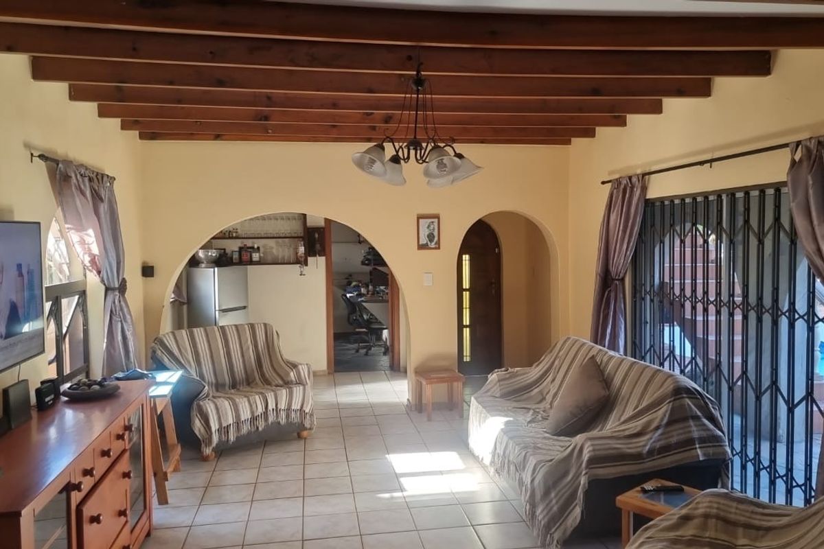 Spacious living room featuring exposed timber ceiling beams, ceramic floor tiles, and arched architectural details leading to adjacent rooms.