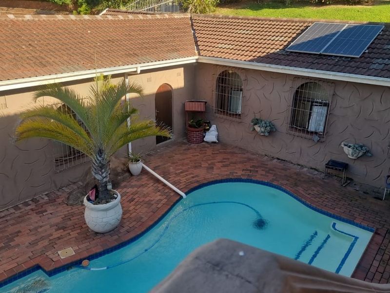 An elevated view of a backyard pool area featuring brick paving, a swimming pool, and a house exterior with solar panels and security bars.
