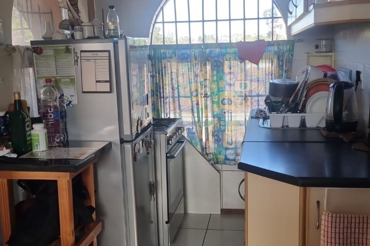 A compact kitchen featuring tiled flooring, built-in cabinetry, and a distinctive arched window with security bars.