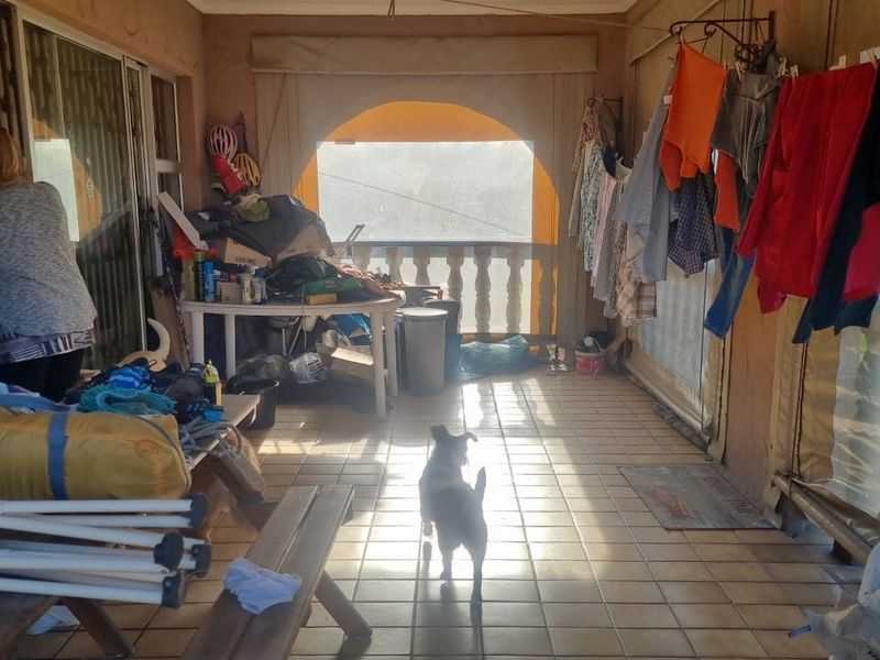 A covered patio area featuring tiled flooring, a decorative balustrade, and sliding glass door access to the main dwelling.