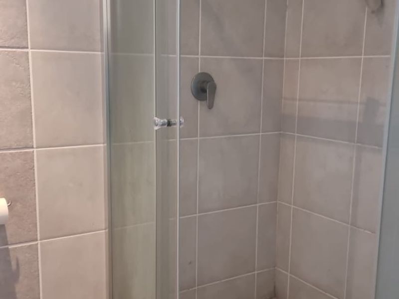 A functional bathroom shower enclosure featuring tiled walls and mosaic floor tiling with a standard shower mixer and head.