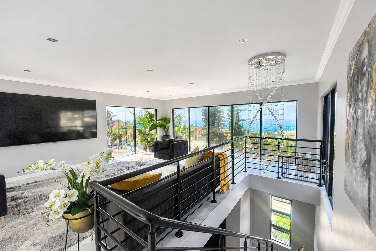 Spacious open-plan living area featuring modern floor tiles, a striking crystal chandelier, and expansive glass doors offering scenic views and abundant natural light.