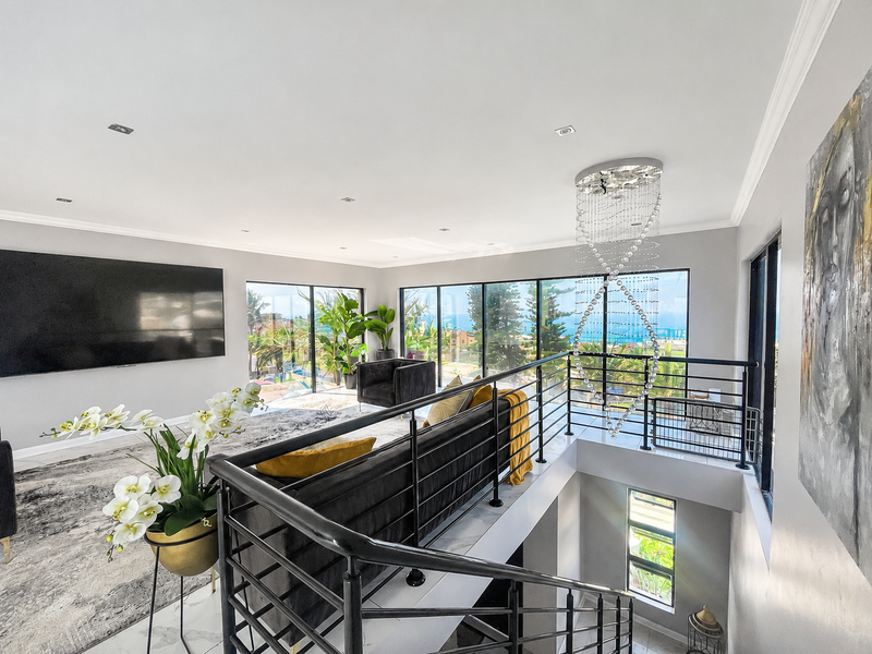 Spacious open-plan living area featuring modern floor tiles, a striking crystal chandelier, and expansive glass doors offering scenic views and abundant natural light.