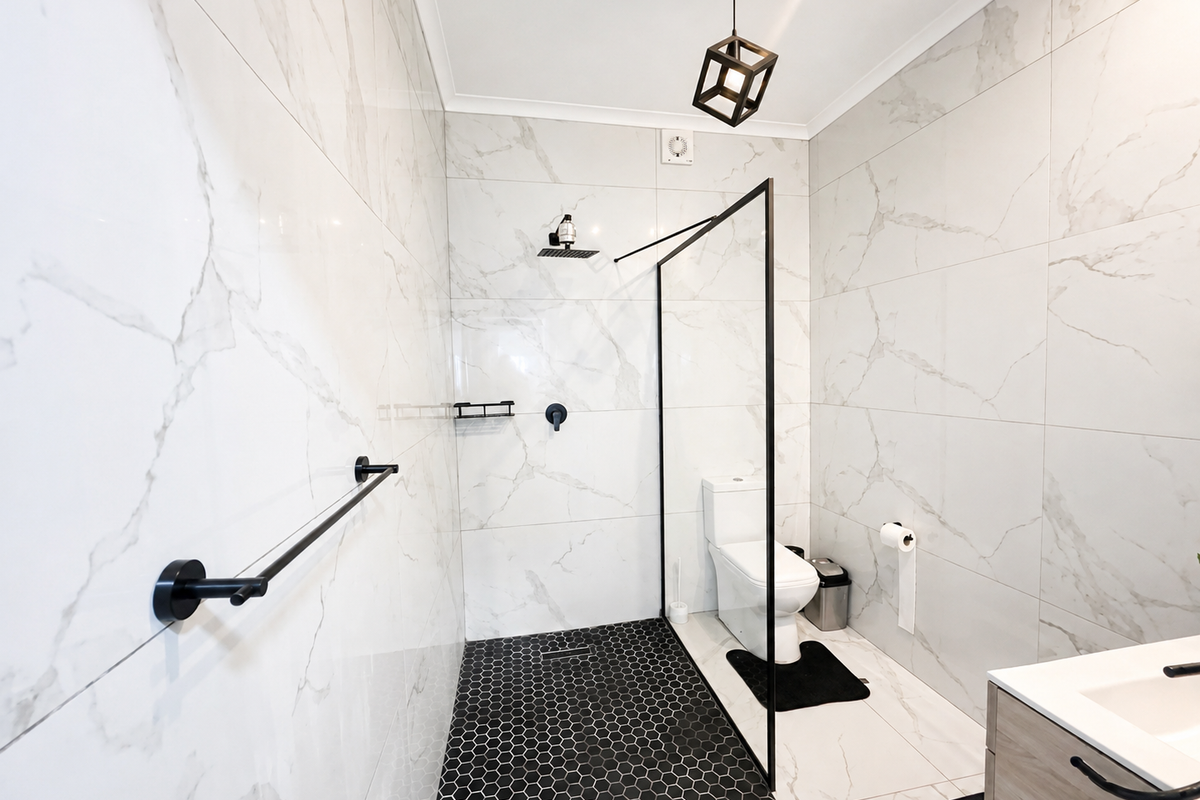 Modern bathroom featuring a walk-in shower with black frame, marble-look wall tiles, black hexagonal floor tiles, and a contemporary vanity unit.