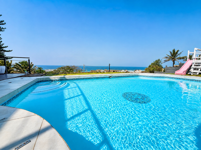 A well-maintained swimming pool featuring integrated steps and a scenic ocean view, complemented by surrounding decking and safety railings.