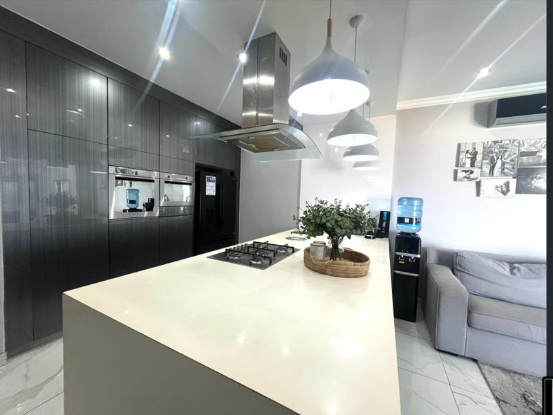 Modern kitchen featuring a large central island with a gas hob, integrated oven, high-gloss cabinetry, and sleek stone countertops.