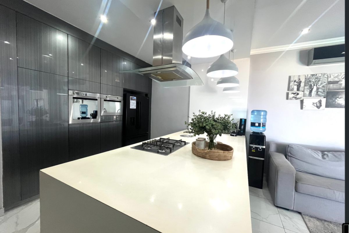 Modern kitchen featuring a large central island with a gas hob, integrated oven, high-gloss cabinetry, and sleek stone countertops.