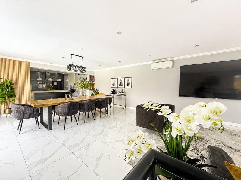 Spacious open-plan living and dining area featuring polished marble-look flooring, modern timber slat wall detailing, and a sleek integrated kitchen.