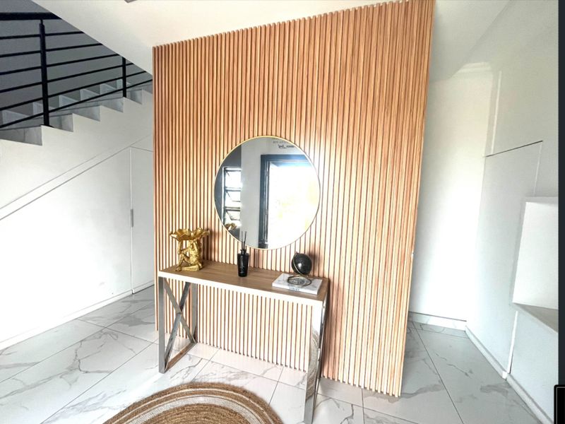 Modern entrance hall featuring a striking vertical slatted timber feature wall, marble-look floor tiles, and a sleek staircase with a contemporary metal balustrade.