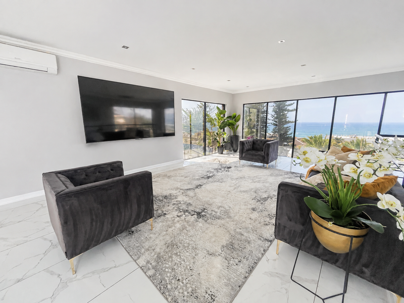 Spacious living room featuring large format floor tiles, recessed lighting, and expansive floor-to-ceiling glass doors offering panoramic ocean views.