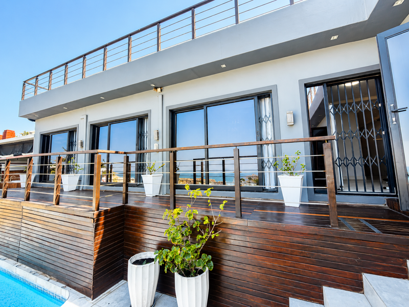 Spacious elevated timber deck featuring modern balustrades, sliding glass doors with security gates, and direct access to the swimming pool area.