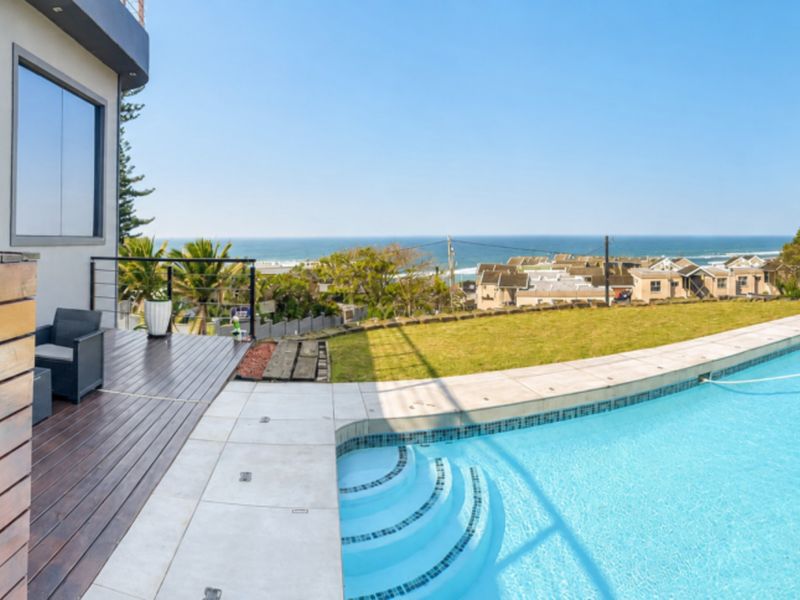Outdoor pool area featuring a swimming pool, timber decking, and tiled surround with scenic coastal views.
