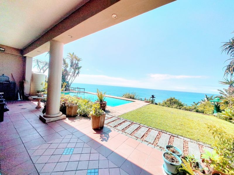 Covered patio area featuring tiled flooring and concrete columns, overlooking a swimming pool, garden, and expansive ocean views.