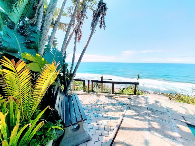An elevated outdoor patio area featuring paved flooring and a timber railing, offering direct, unobstructed views of the ocean and coastline.