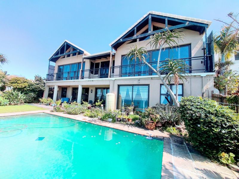 Rear view of a double-story house featuring a swimming pool, a spacious balcony, and large sliding glass doors opening to the garden.