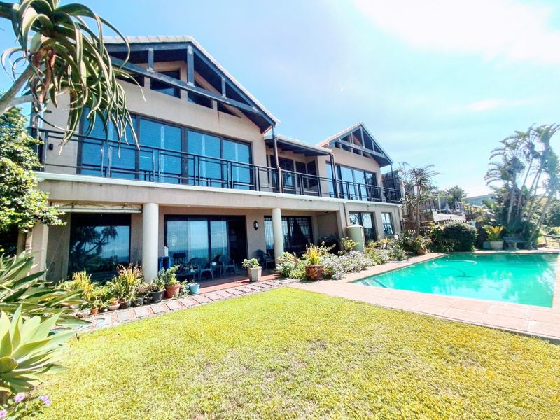 Rear elevation of a double-story residence featuring a swimming pool, paved patio area, and upper-level balcony with sliding glass doors.