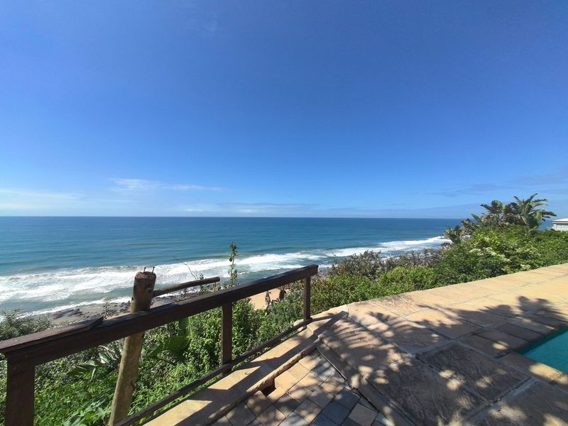 Stunning elevated ocean view featuring a stone-paved pool deck and timber safety railing overlooking the coastline.