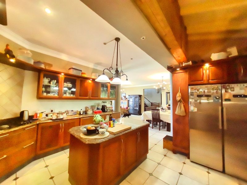 Spacious open-plan kitchen featuring warm wooden cabinetry, stone countertops, a central island, and tiled flooring, flowing seamlessly into the adjacent dining area.