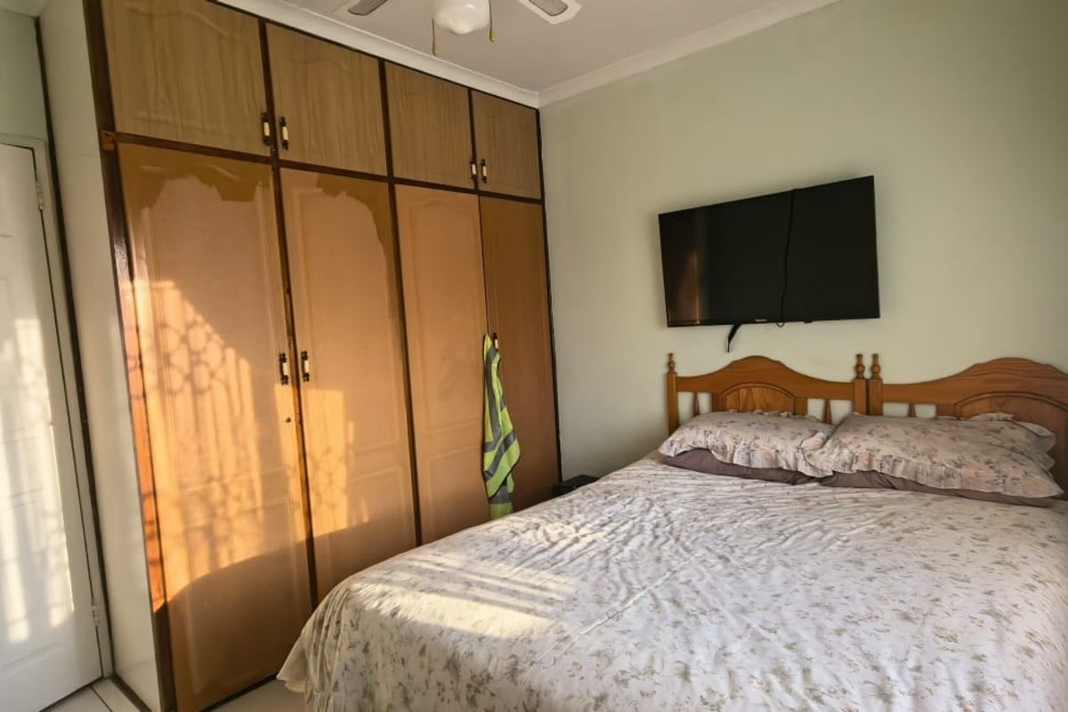 A bedroom featuring built-in wooden cupboards, a ceiling fan, and coving, offering a functional space with potential for cosmetic updates.