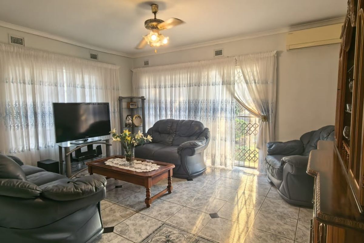 A spacious living room featuring tiled flooring, a ceiling fan, and split-system air conditioning, with large windows providing ample natural light.
