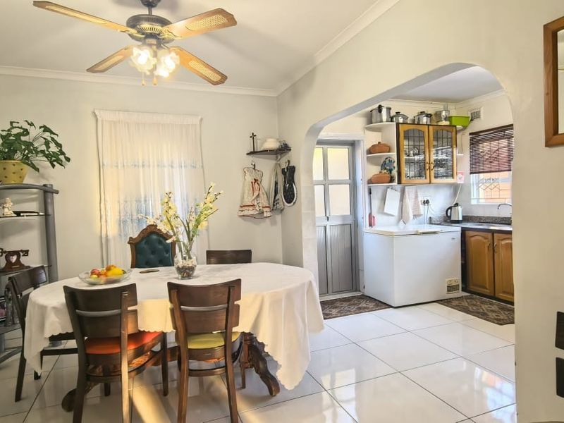 Open-plan dining area featuring tiled flooring and a ceiling fan, flowing into a functional kitchen space with wooden cabinetry and stone countertops.