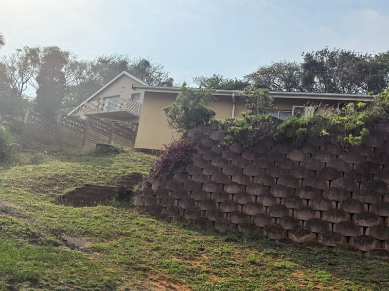 Rear view of the property featuring a large tiered retaining wall, landscaped garden area, and an elevated balcony.
