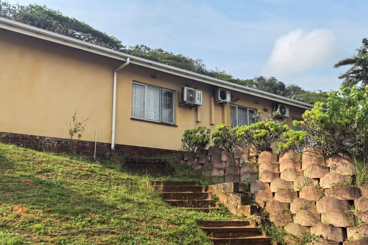 Rear exterior view of the house featuring a sloped garden, concrete retaining wall, and external air conditioning units mounted on the wall.